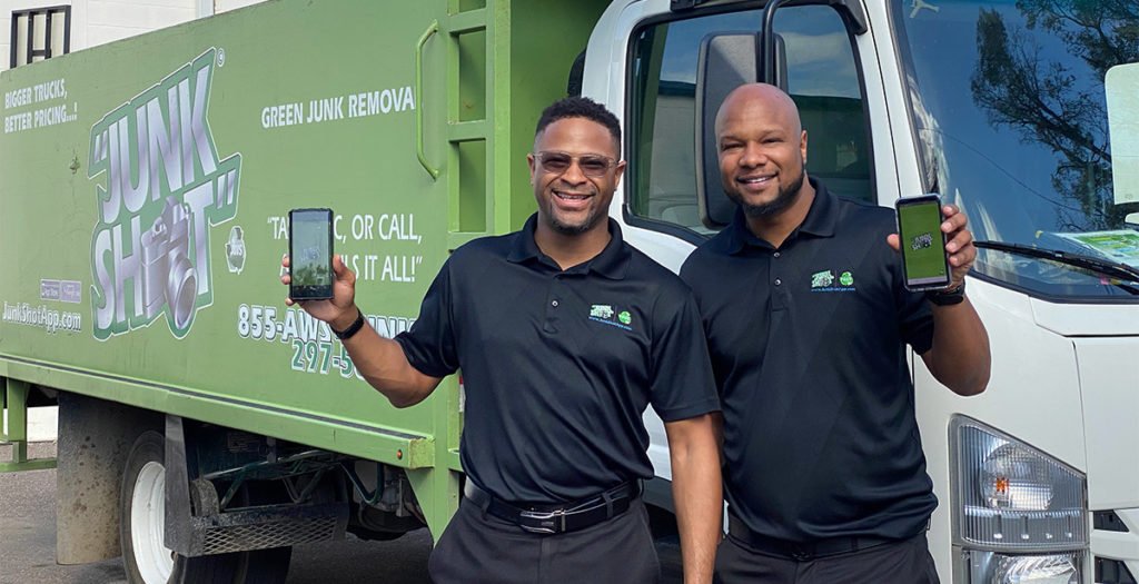 Junk removal franchise owners holding app on phone in front of junk shot truck